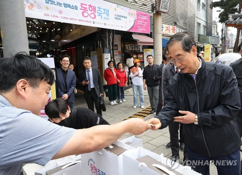 한덕수 국무총리(오른쪽)가 20일 서울 종로구 통인시장을 방문해 상인들을 격려하고 구매 영수증으로 사은행사에 참여하고 있다.